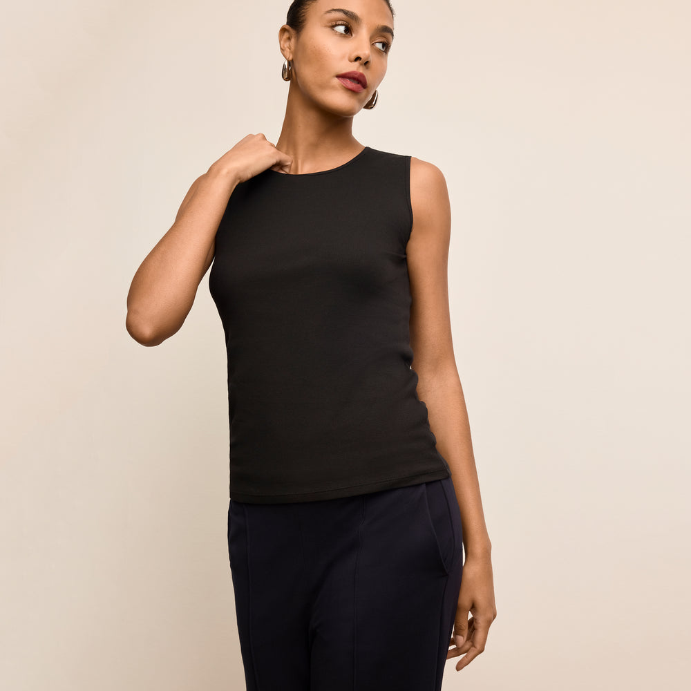 Woman wearing a black sleeveless top and dark pants against a beige background