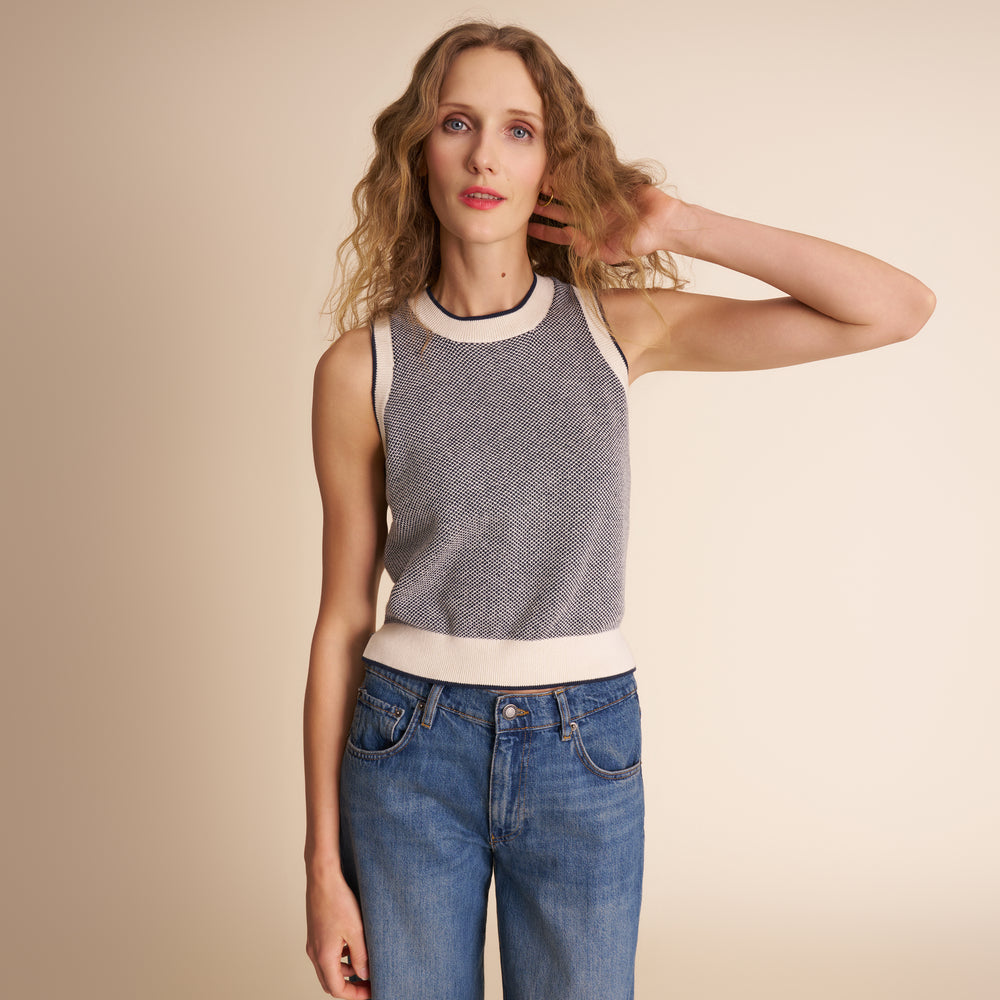 Woman wearing a sleeveless patterned top and blue jeans against a beige background