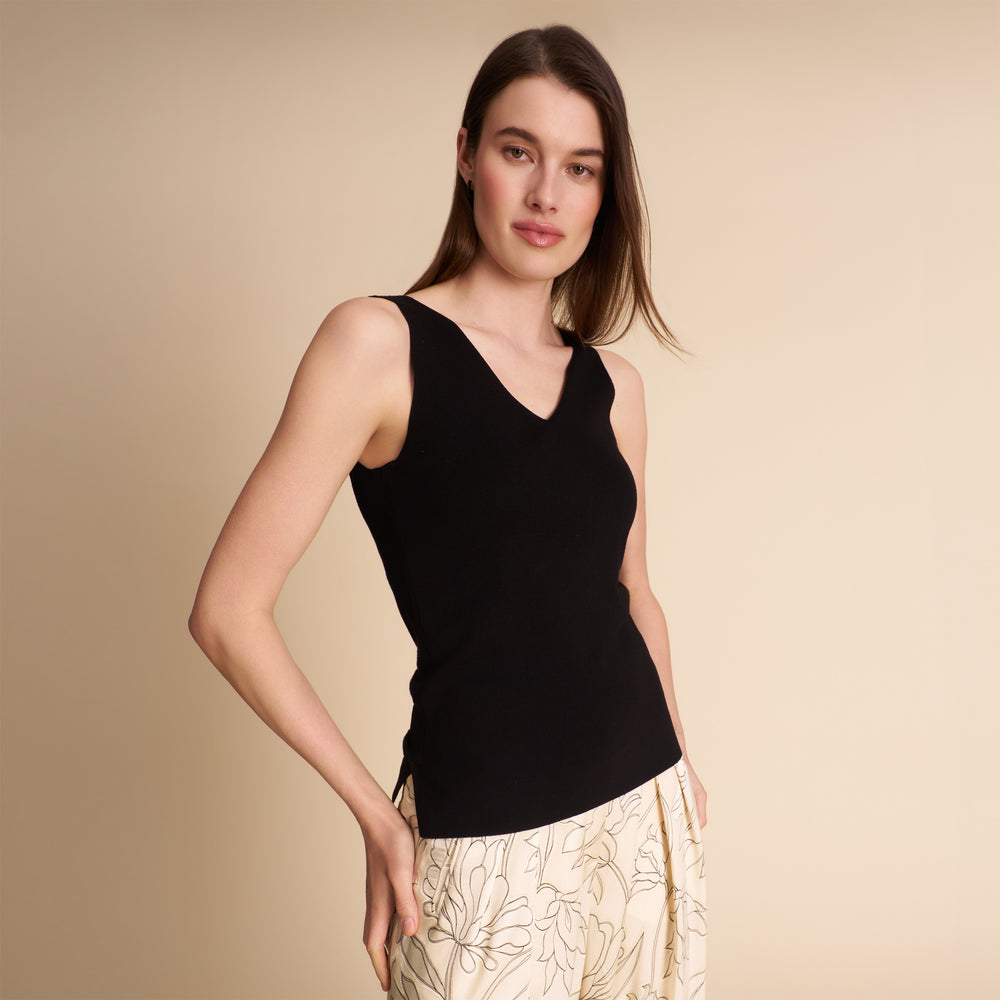 Woman wearing a black sleeveless top and beige pants against a plain background