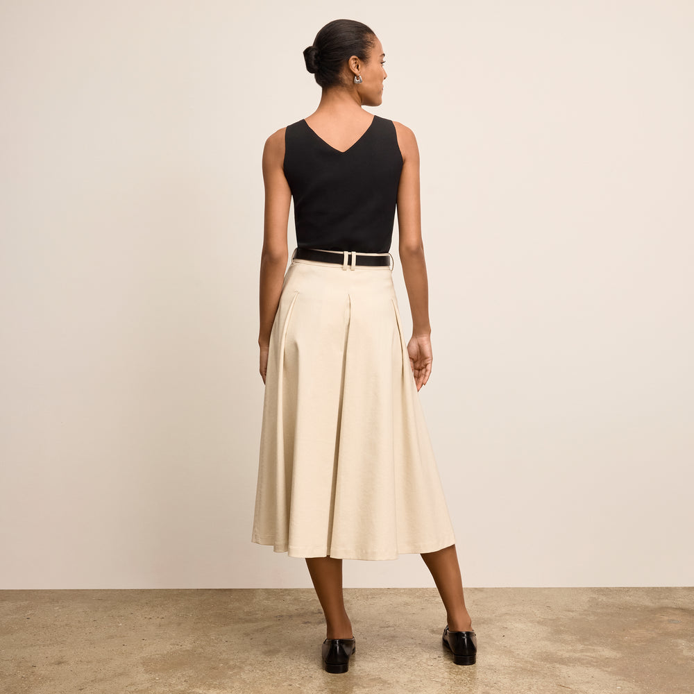 Woman wearing a black top and beige skirt against a plain background