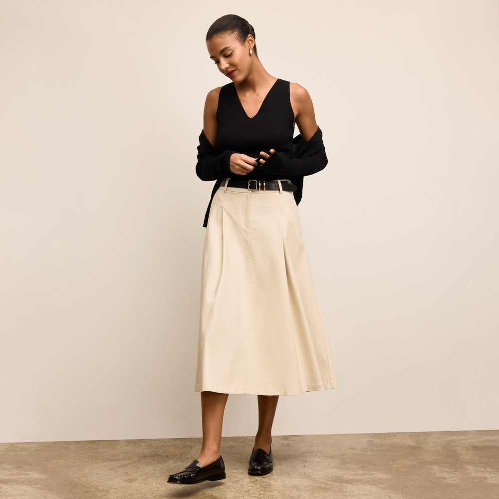 Woman wearing a black top and beige skirt against a plain background