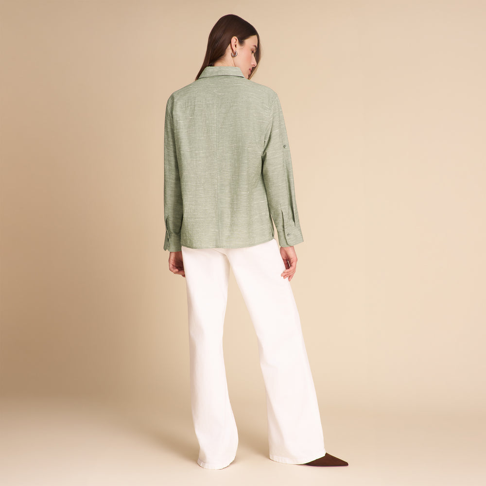 Woman wearing a green jacket and white pants on a beige background