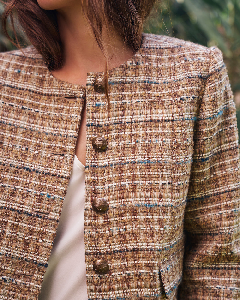 Close-up of a woman wearing a brown tweed jacket with blue and beige striped details, featuring three large brown buttons down the front.