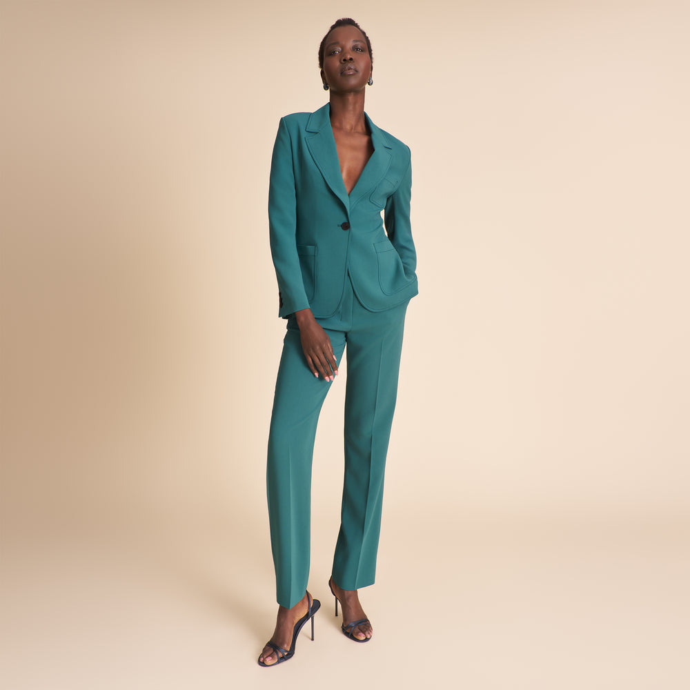 Woman wearing a teal pant and jacket suit on a beige background
