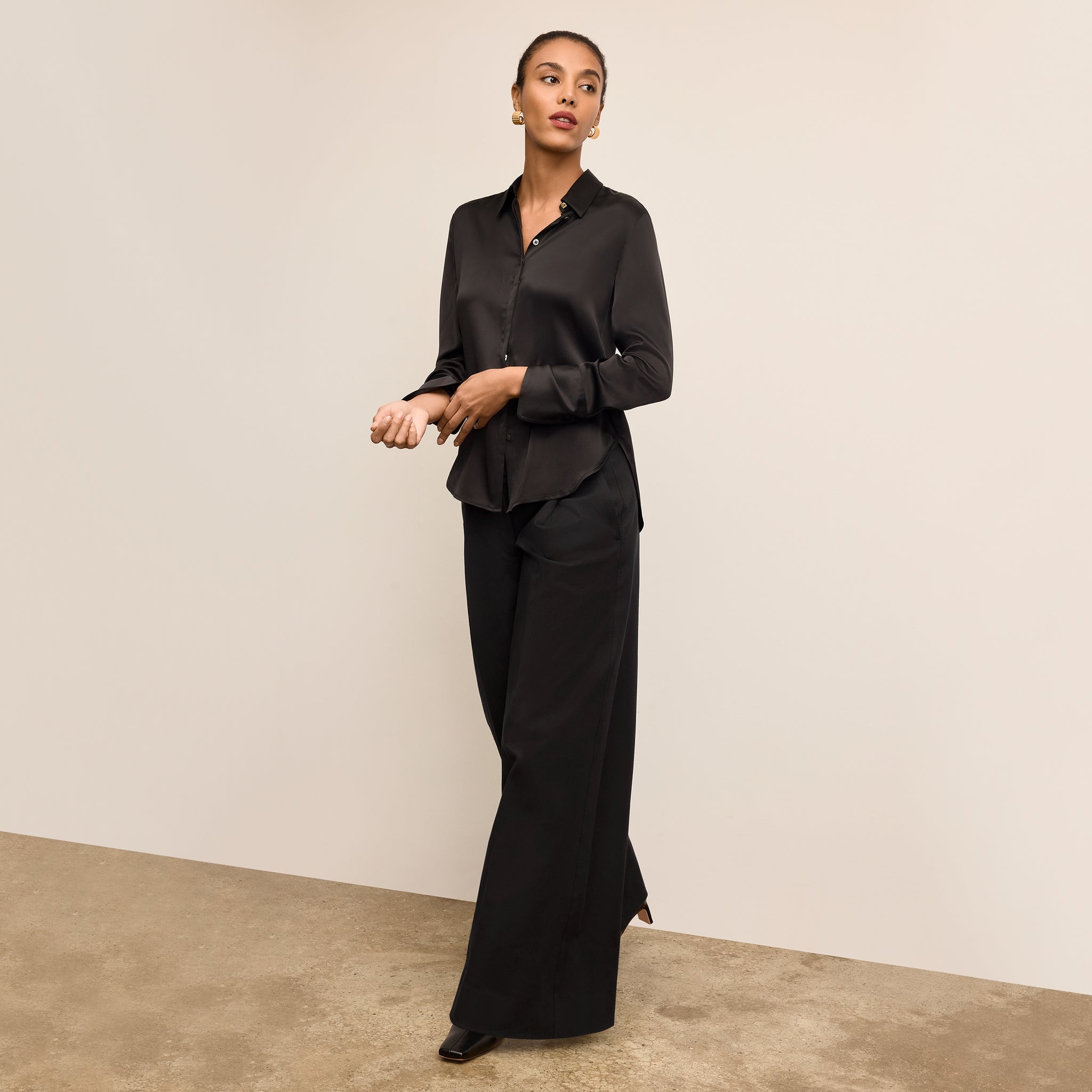 Woman wearing a black suit standing against a beige wall. 