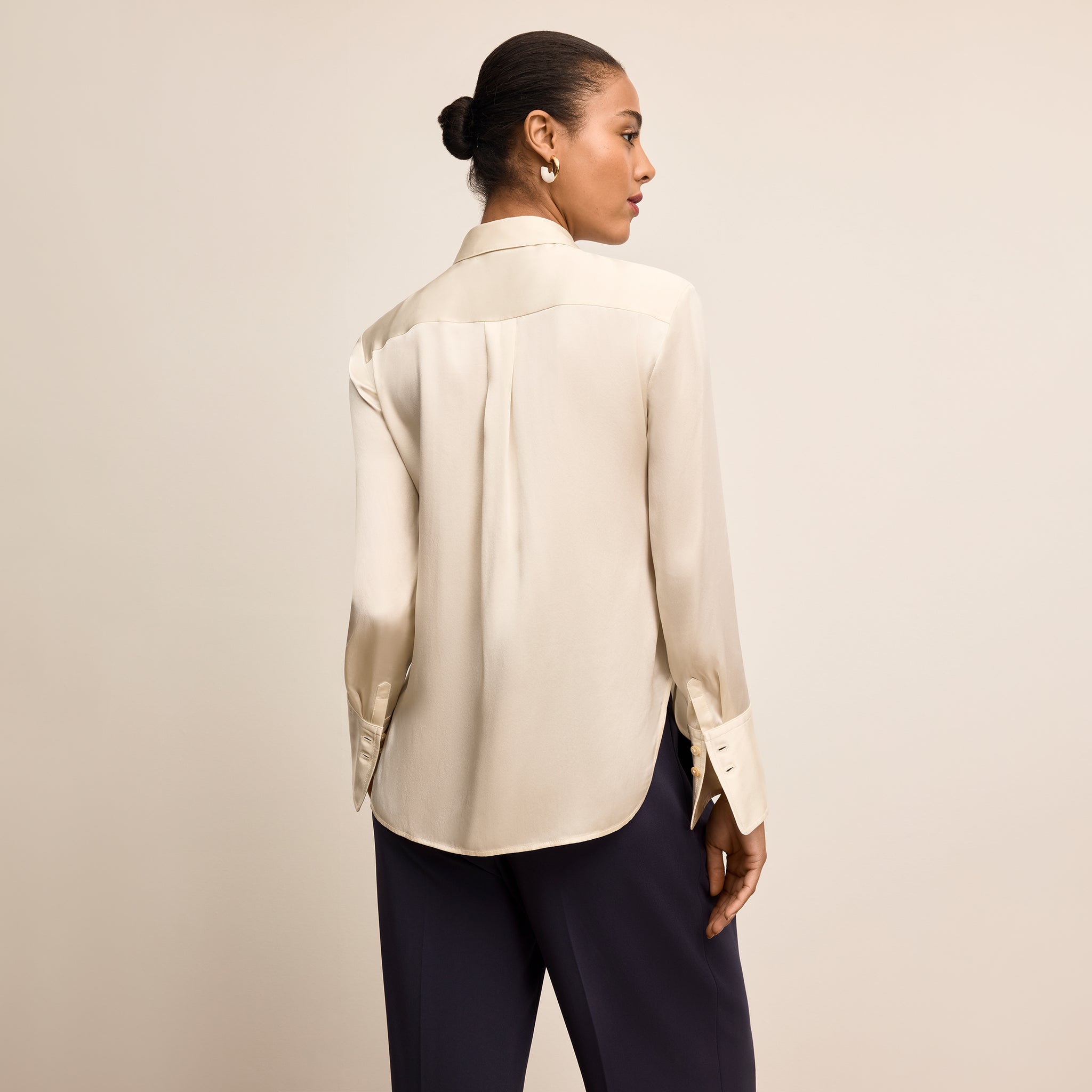 Woman wearing a beige satin blouse and navy pants against a beige background