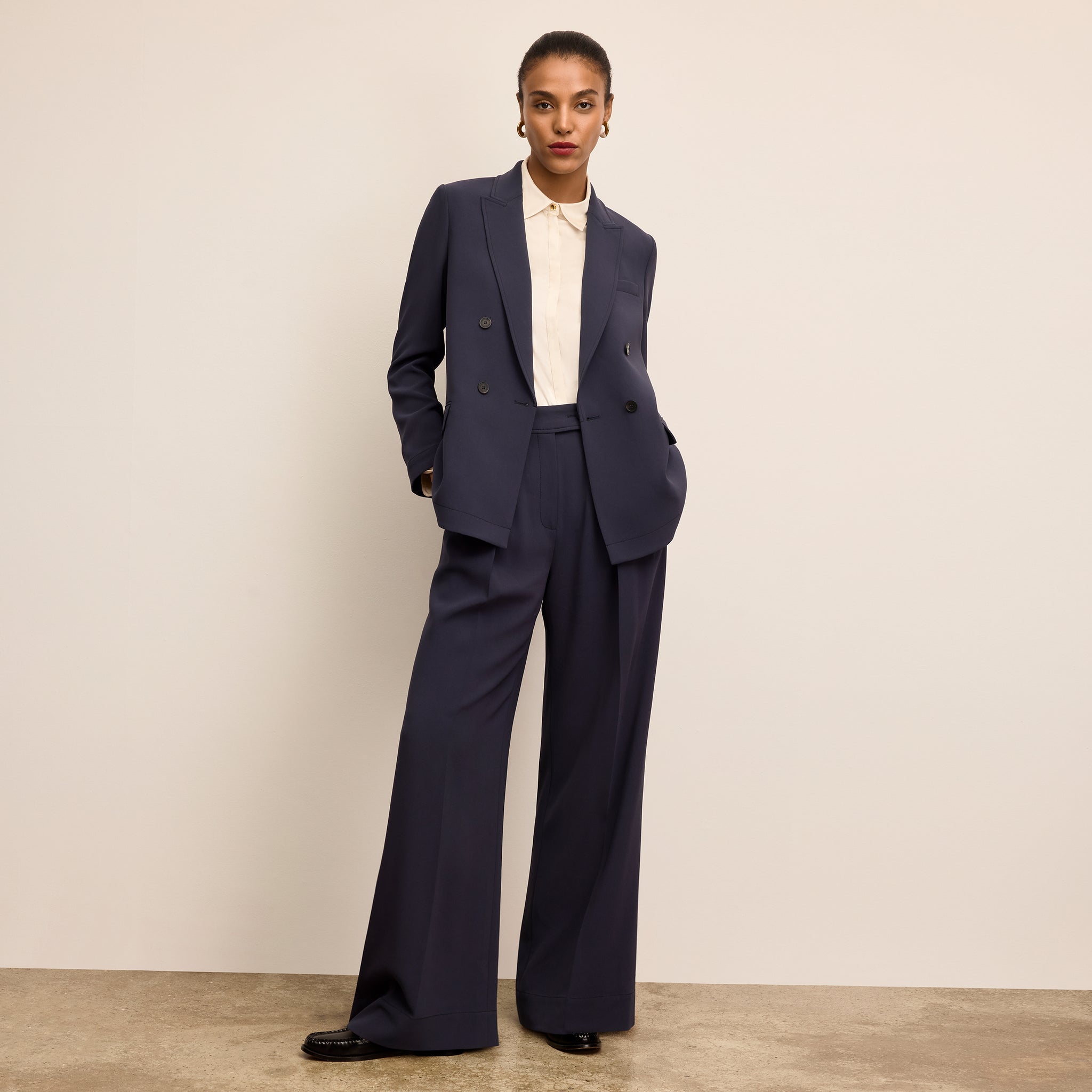 Woman wearing a navy suit with a white shirt against a beige background