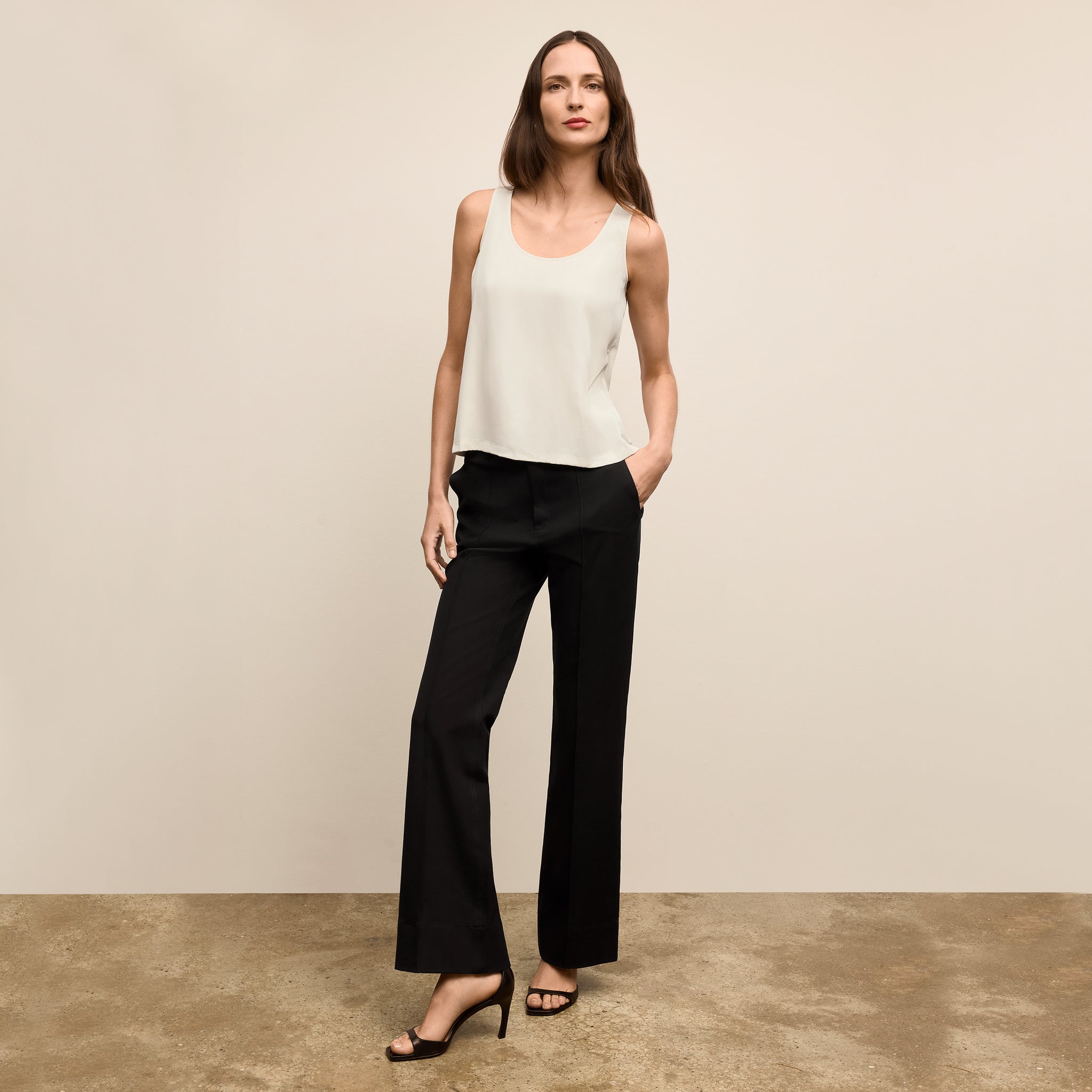 Woman wearing a white sleeveless top and black pants against a beige background 