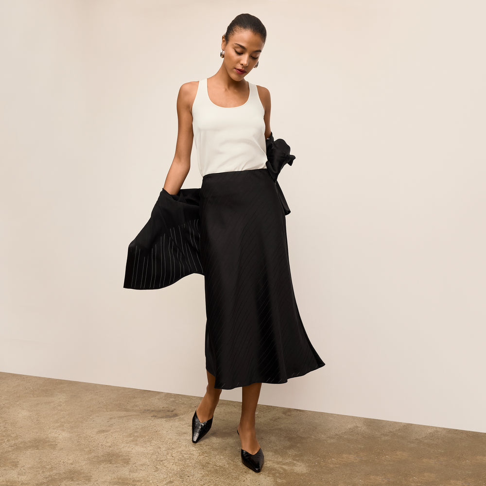 Woman wearing a white top and black skirt against a plain background