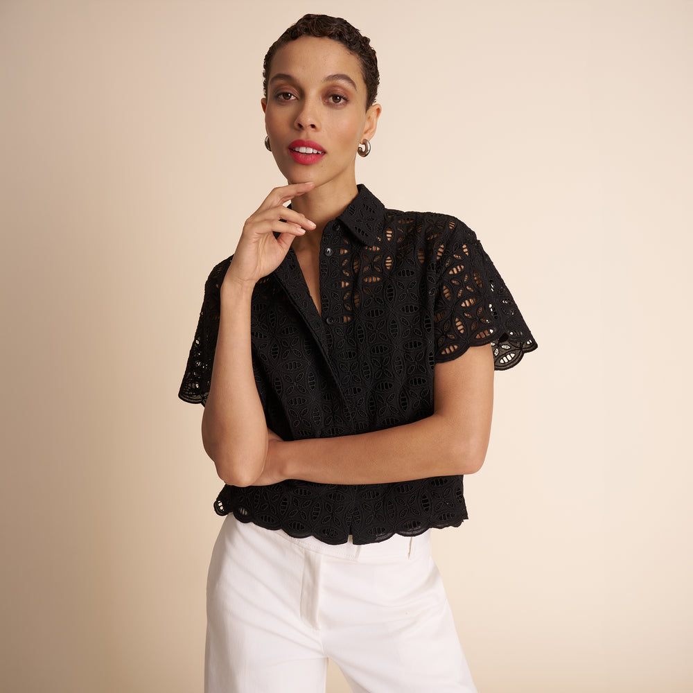 Woman wearing a black lace top and white pants against a beige background