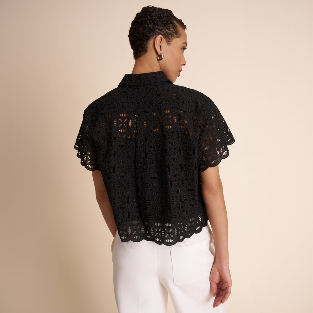 Woman wearing a black lace top and white pants against a beige background