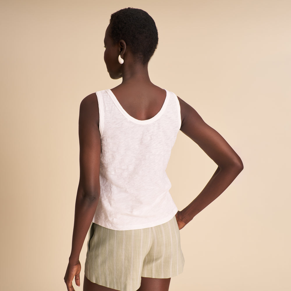 Woman wearing a white tank top with striped beige and mauve shorts on a beige background