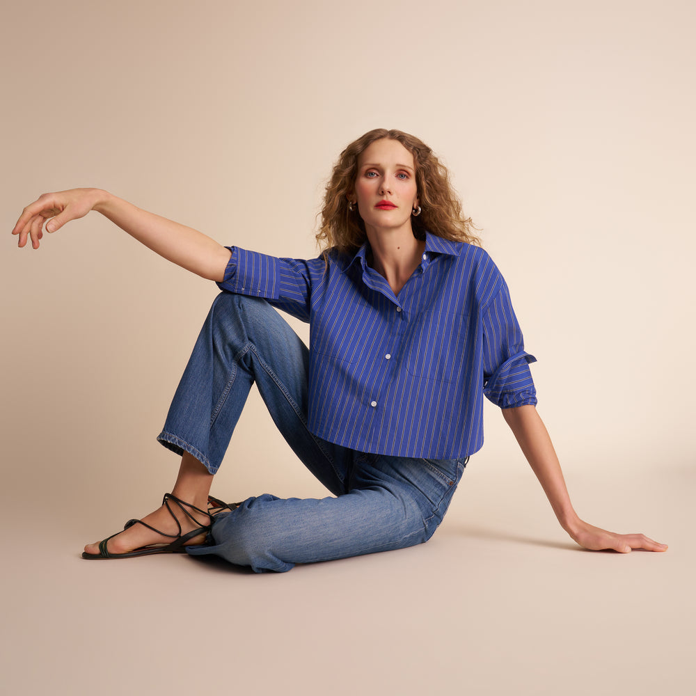 Woman wearing a blue striped shirt and jeans sitting on a beige background