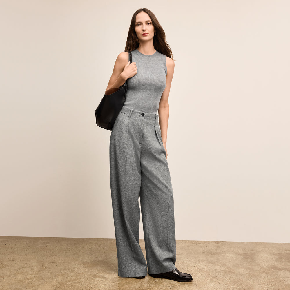 Woman wearing a gray sleeveless top and wide-leg pants holding a black handbag against a beige background