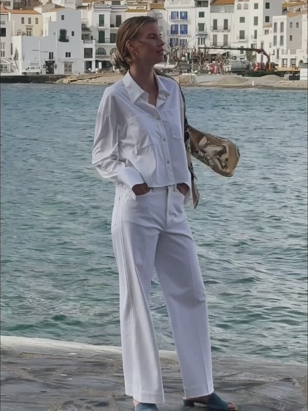 Woman walking on a beach with a scenic coastal town in the background.