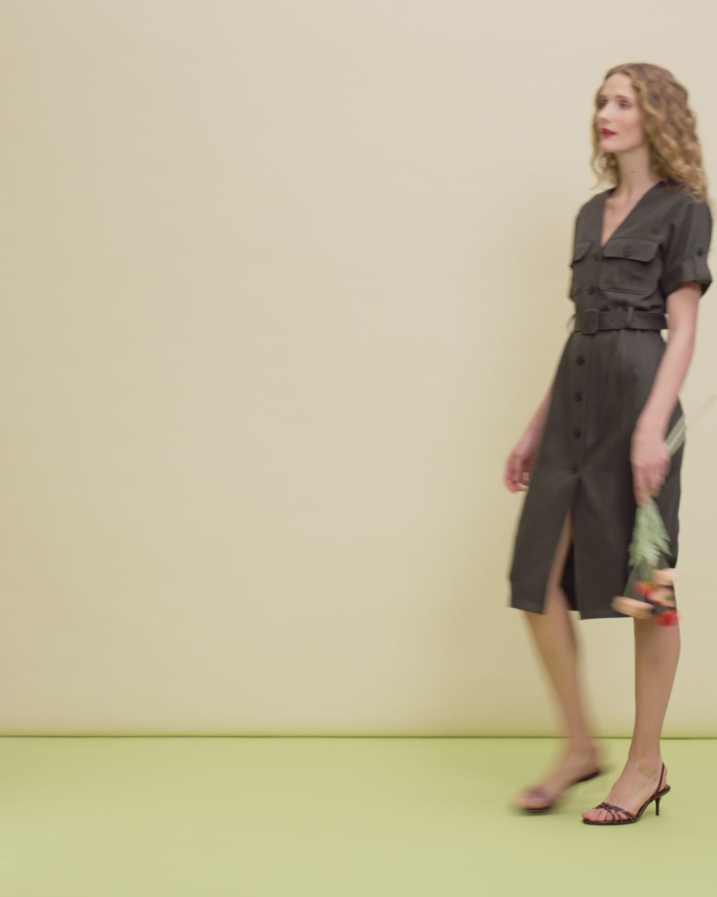 Woman wearing a green dress with a belt on a beige background.