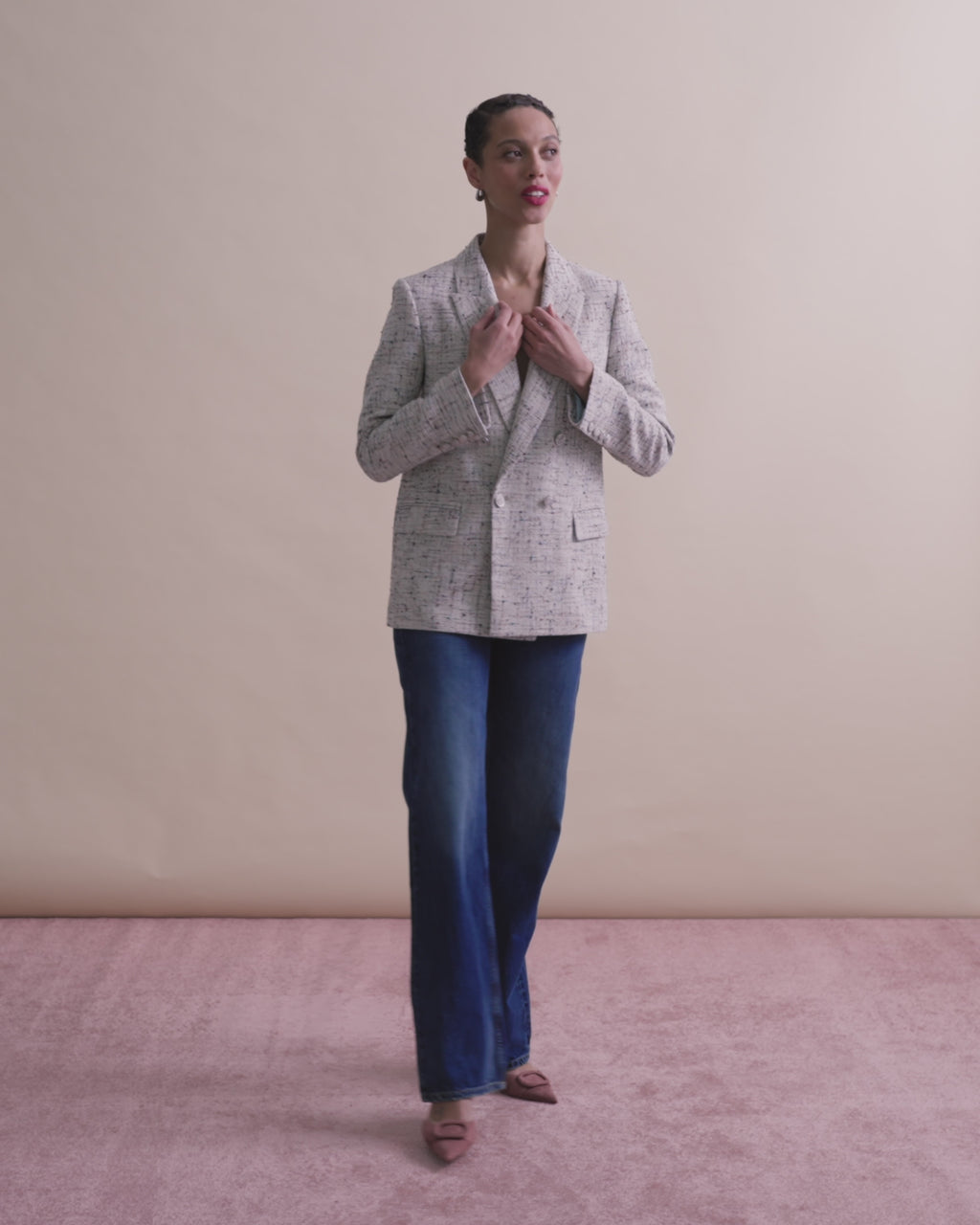 woman in blazer and jeans with pink background.